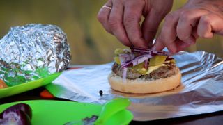 A person wrapping a cheeseburger in foil