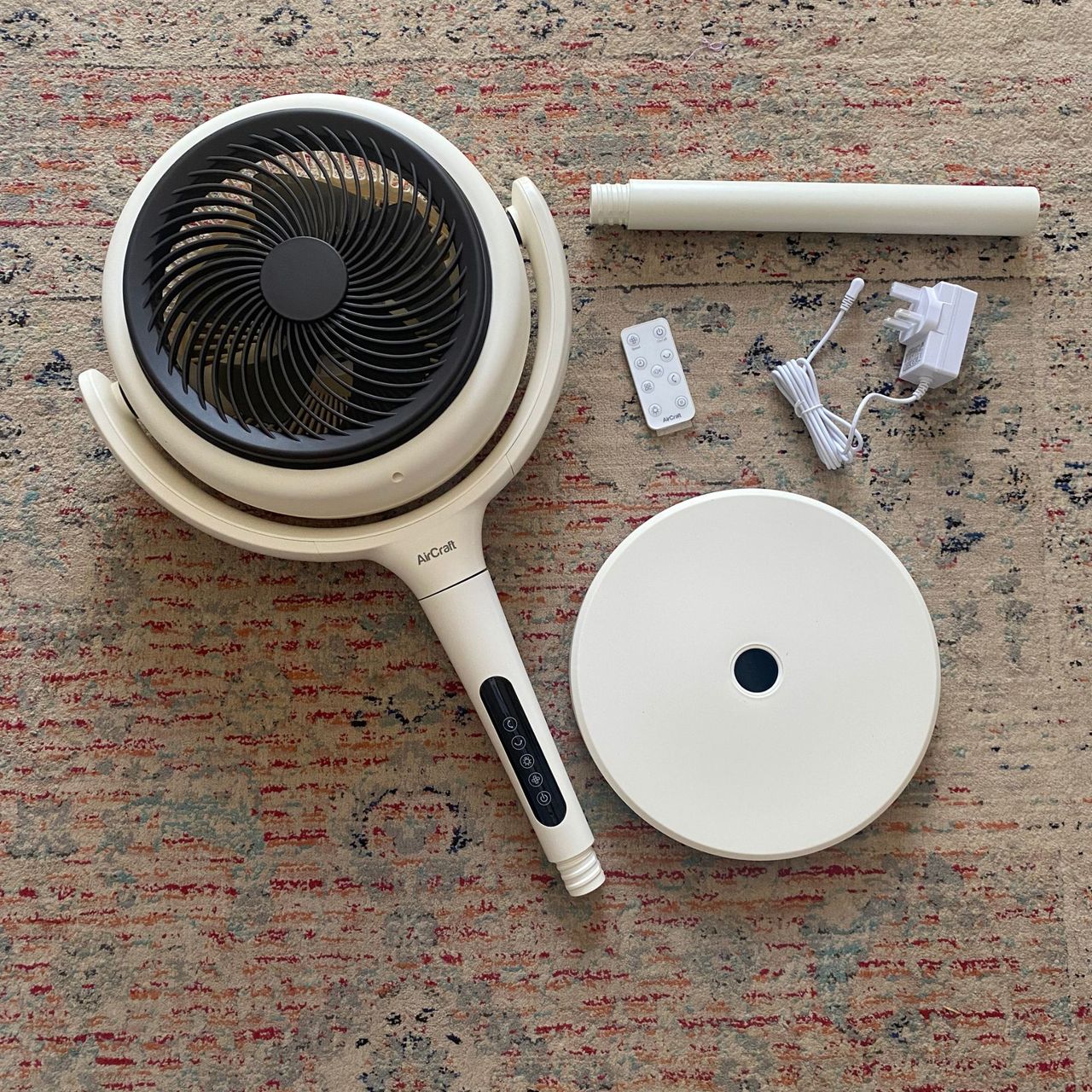 Flat lay of what you get in the box of the AirCraft LUME Quiet Air Circulator Fan on a beige, red and grey patterned rug