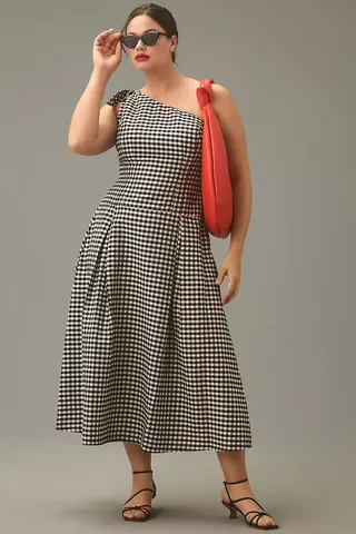 model is wearing gingham dress and red handbag with black kitten heels and sunglasses looking off into the distance