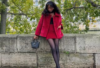 Emmanuelle is wearing a red velvet jacket, red velvet skirt, black top, black sheer tights, black ballet flats, black top-handle bag.