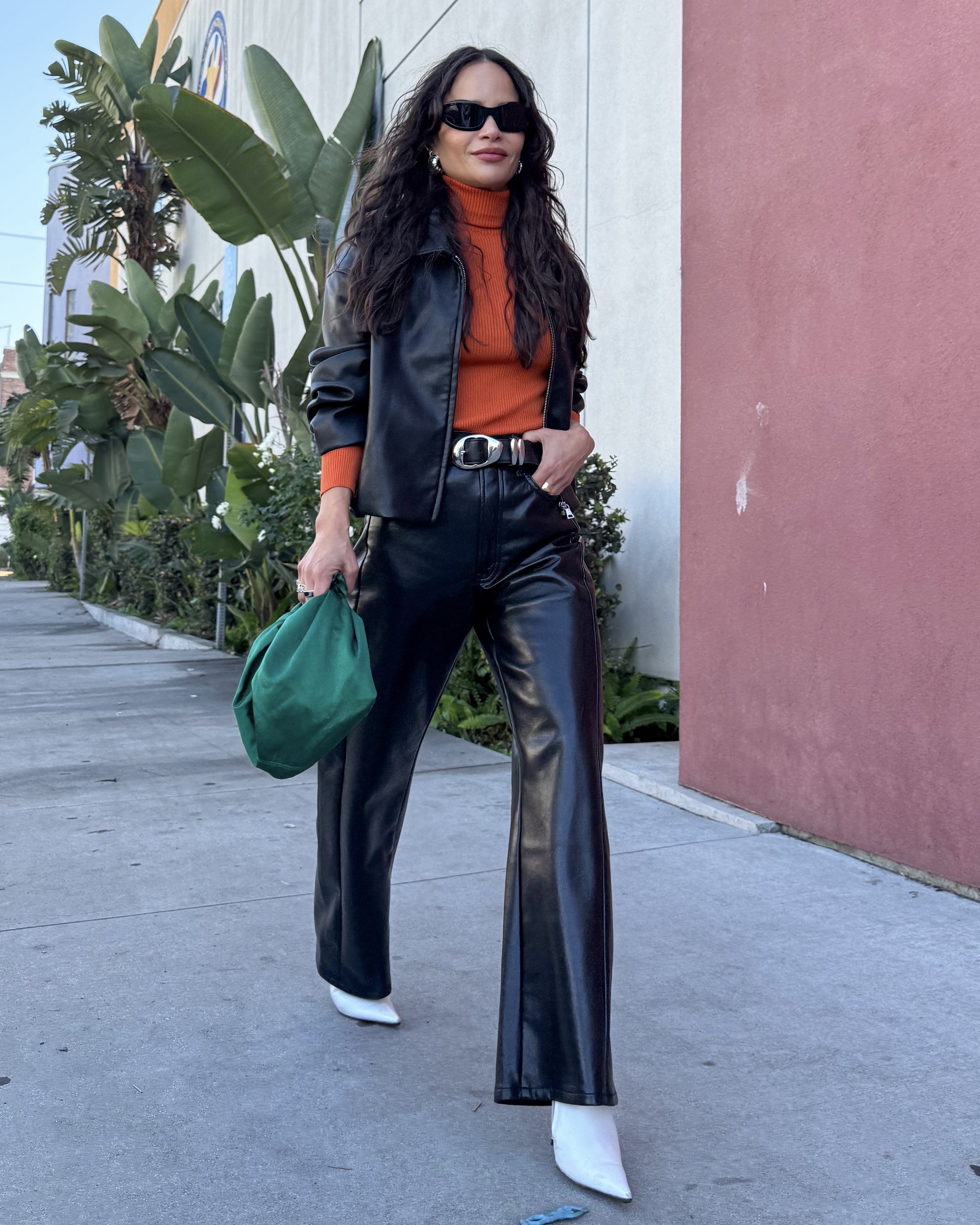 Sophie Lopez wearing a cropped leather jacket, and orange shirt, leather pants, white heels, and a green bag