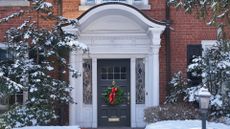 A home with a Christmas wreath hanging outside its door as snowy foliage wraps around it 