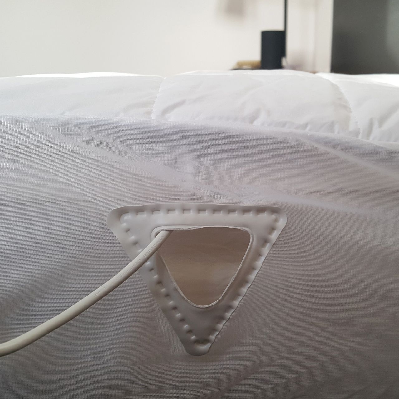A reinforced triangular cut out in the fitted skirt of the Dreamland Snowed In Dual Control Heated Mattress Protector with the blanket's white power cable going through it