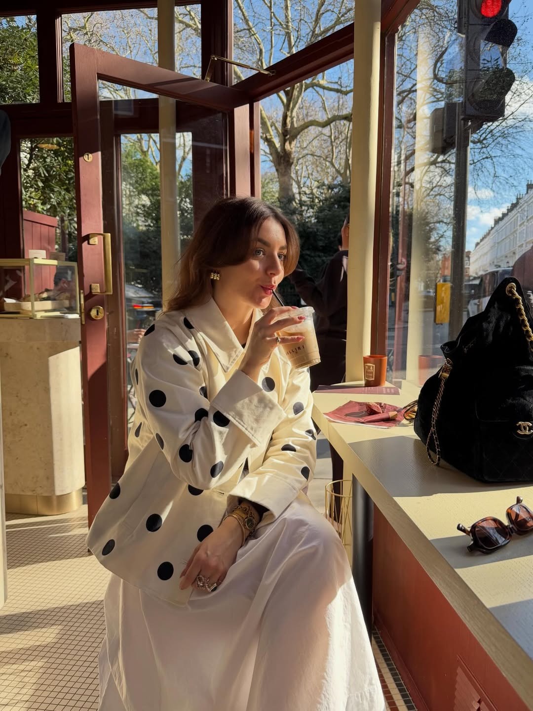 Woman wears a polka dot jacket, white cotton skirt and drinks coffee