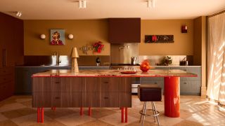 A modern kitchen with a kitchen island with vibrant lacquer red legs and a large circular leg on the seating side, with wood cabinetry and oxblood and blue cabinets against a mustard wall
