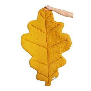 A hand holding a yellow fall leaf rug