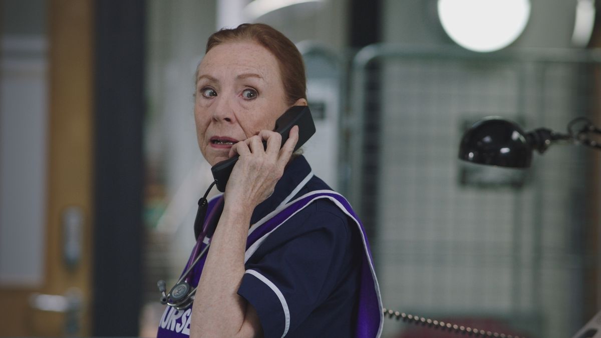 Siobhan McKenzie in her navy uniform on the phone and looking horrified. 