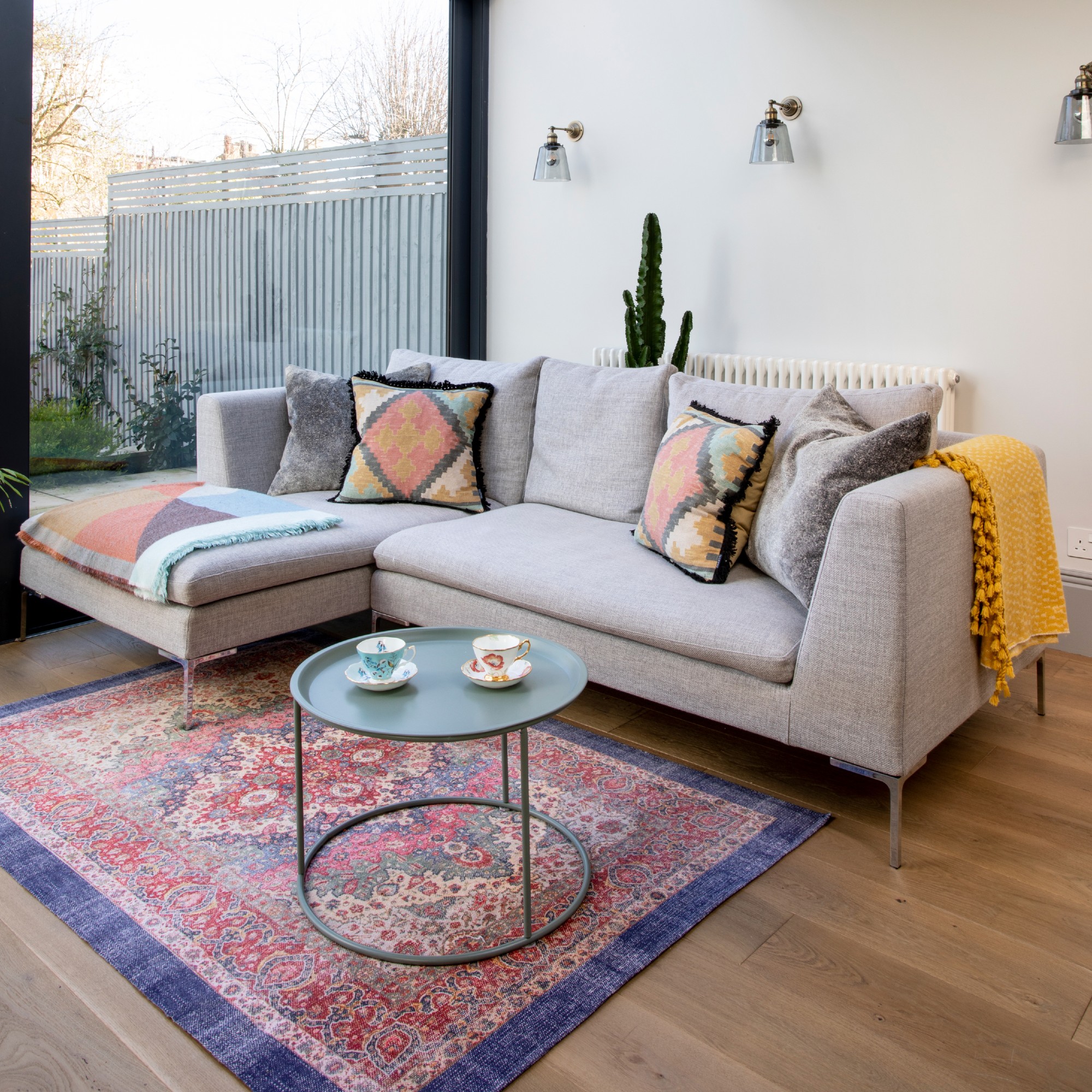 An open-plan living room with with a grey chaise sofa positioned away from the wall with a cactus behind it