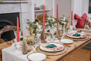 A dining table laid for Christmas dinner with red candles and Christmas decor