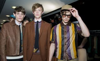 Three male models wearing casual clothing by Salvatore Ferragamo in various colours.