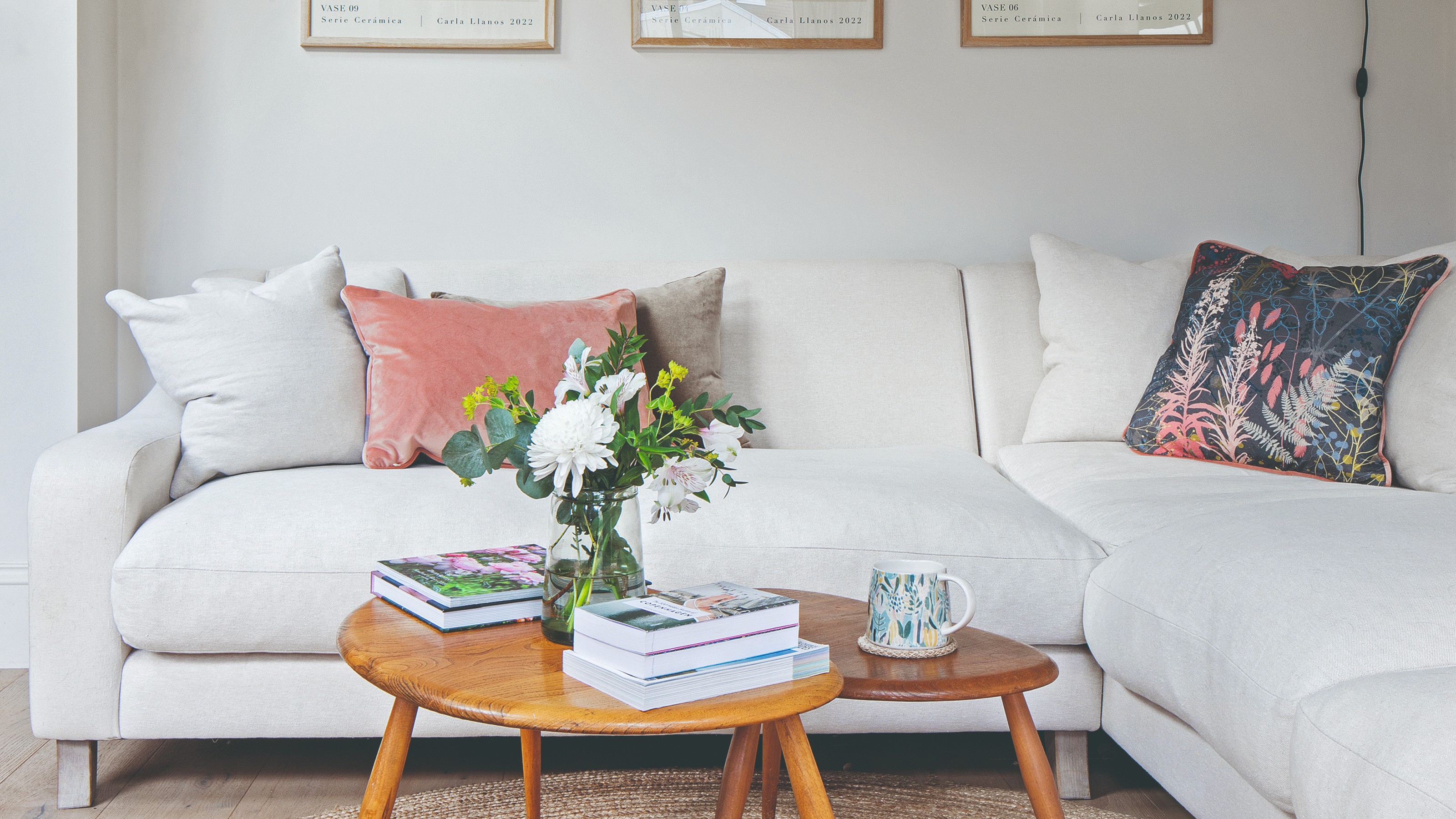 A white living room with a white corner sofa and vintage nesting tables with a vase of flowers on top