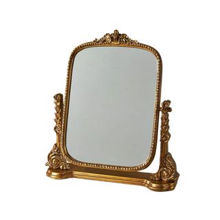 A brushed gold vanity standing mirror with ornate detailing