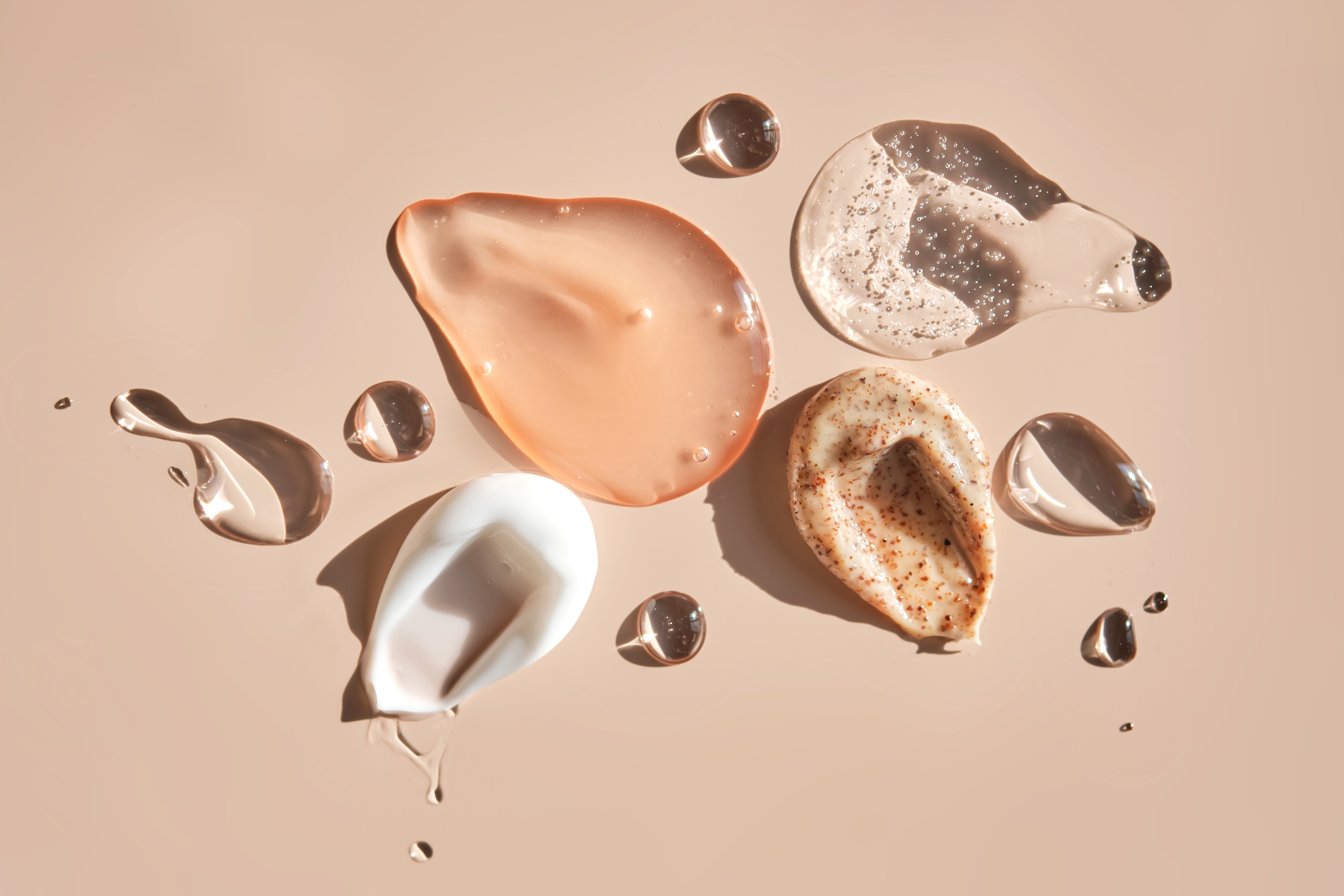 Different cosmetic textures on a delicate peach background. The photo shows a cosmetic gel, serum, cream, facial scrub, micellar water and serum with acids.