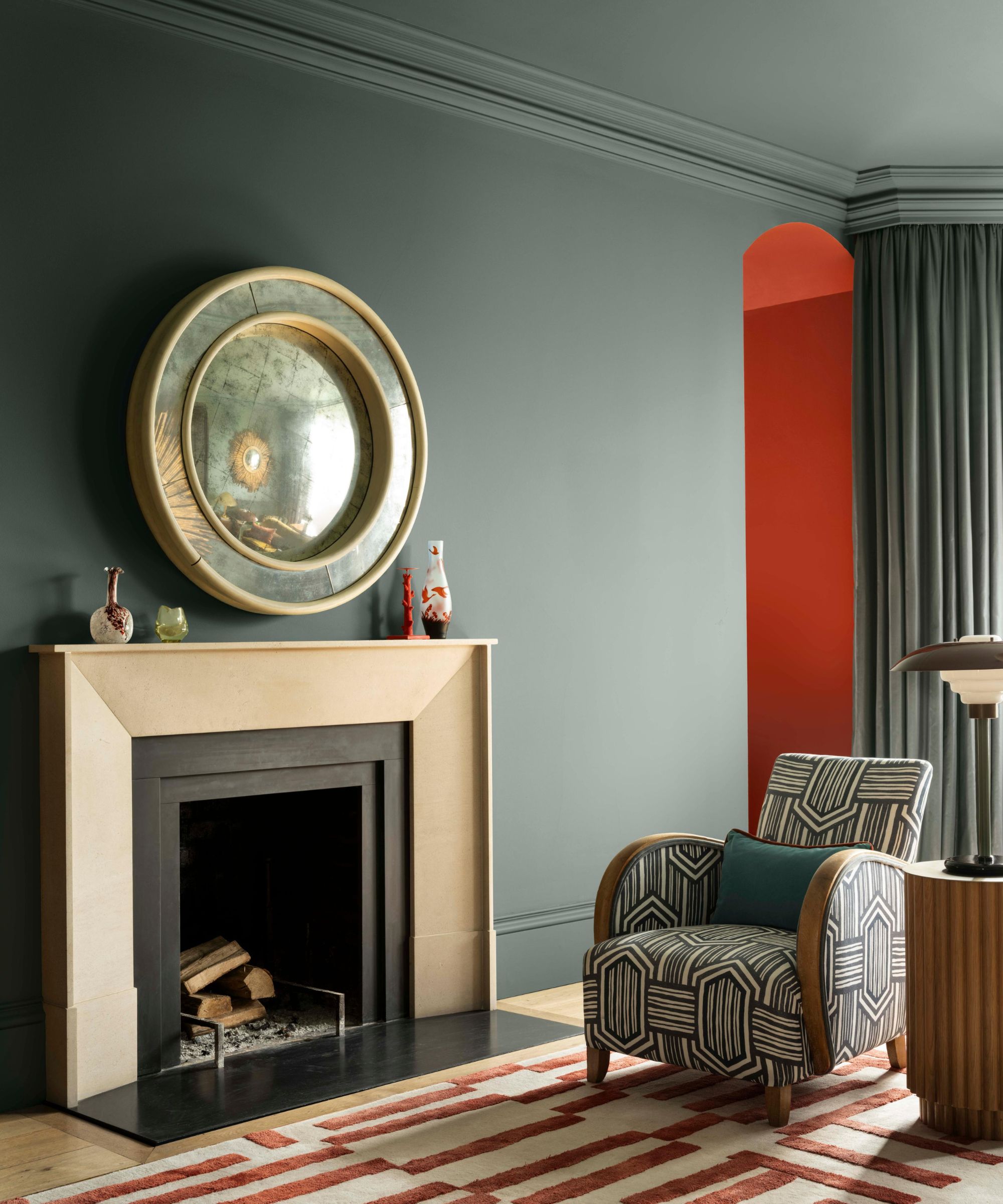 Living room with Blue Spruce walls, a large fireplace with a geometric red-and-white rug, a midcentury armchair upholstered in a geometric print, and an arched doorway painted red.
