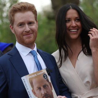 Prince Harry and Meghan Markle impersonators Rhys Whittock and Sarah Mhlanga posing with a copy of Spare