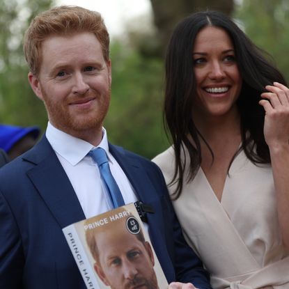 Prince Harry and Meghan Markle impersonators Rhys Whittock and Sarah Mhlanga posing with a copy of Spare