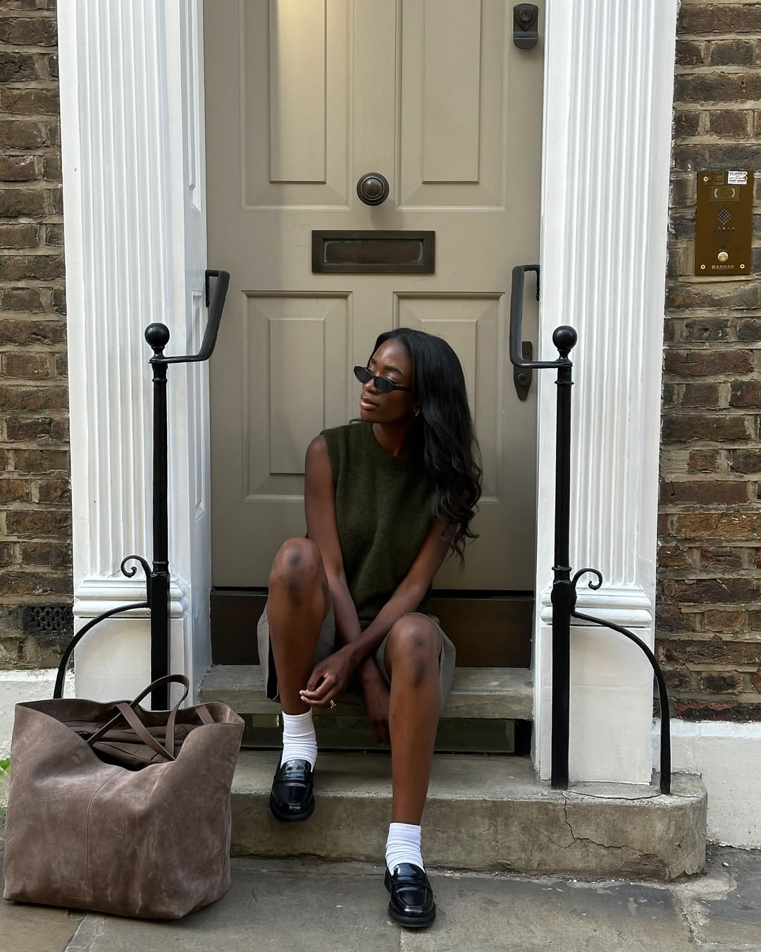 @_livmadeline wears classic penny loafers with a khaki knit vest, Bermuda shorts and suede tote bag