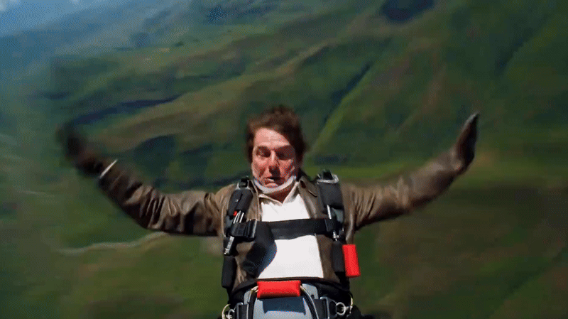 POV footage of Tom Cruise falling backwards out of a moving helicopter, down towards green fields 