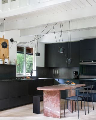 Sleek black handleless kitchen with pink marble island-cum-dining table