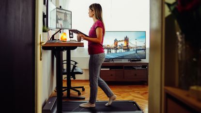 A woman on a walking treadmill working at an elevated desk