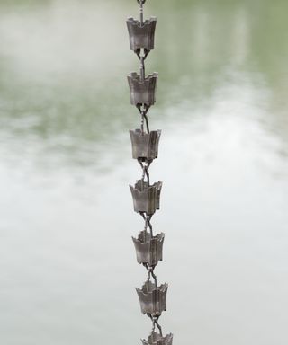 A silver Japanese rain chain hanging in front of a body of water