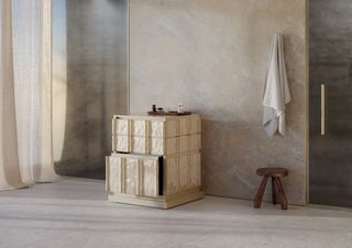 A cream undercounter fridge design in a bathroom with a wooden stool and a towel hanging on the wall