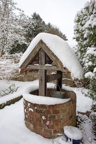 A brick well with thatch roof and snow around it