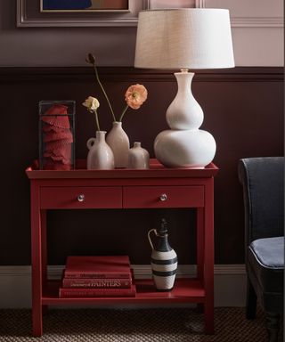 red console table in a hallway with dark red alls below dado and dusky pink above