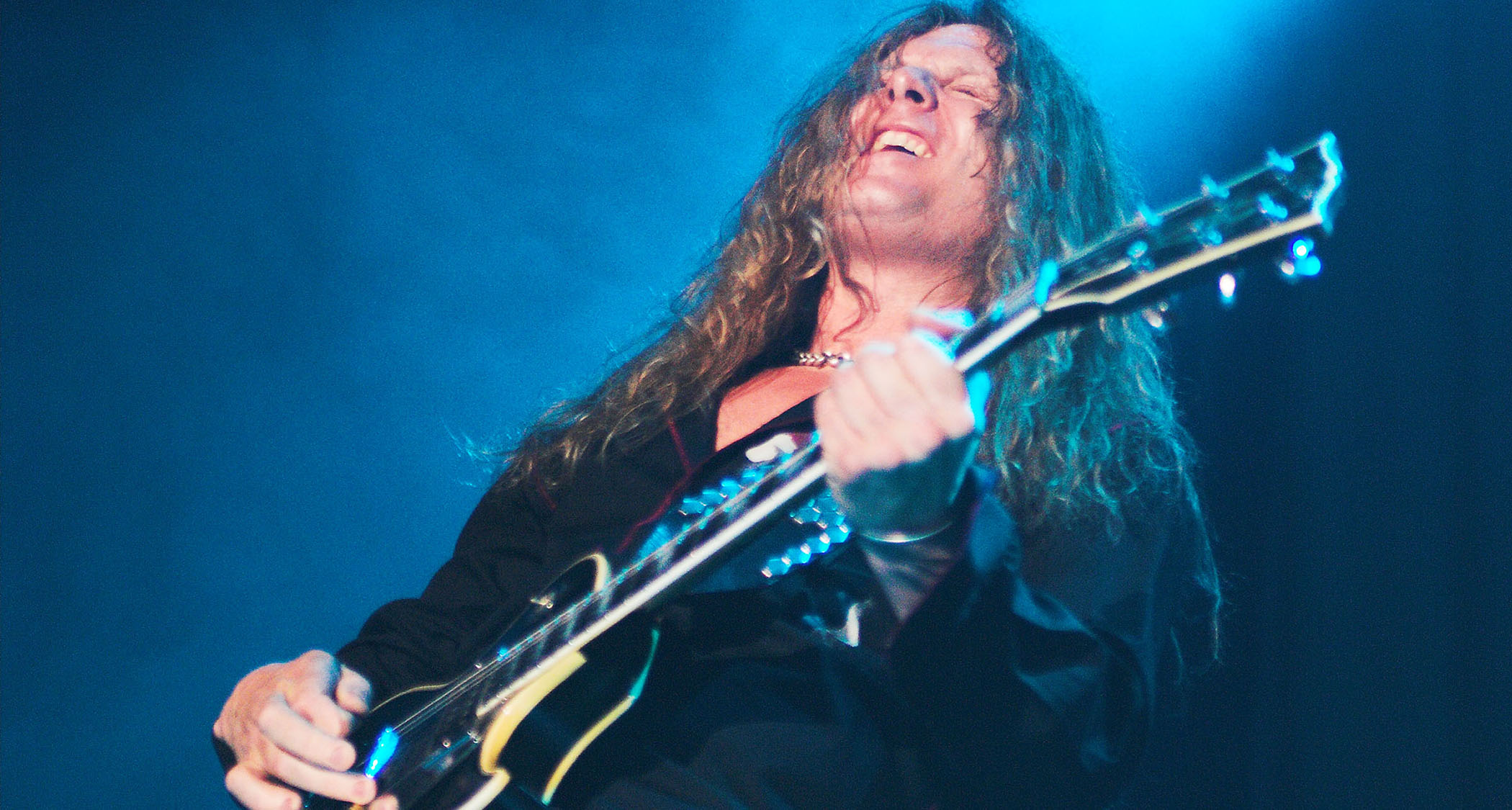 John Sykes hits a note and feels it under a blue stage light, as he plays his Les Paul Custom onstage with Thin Lizzy.