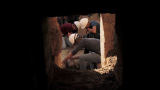 Looking out from a cave, we see three archaeologists wearing hard hats as they work on the Salome’s cave and its forecourts excavation site.