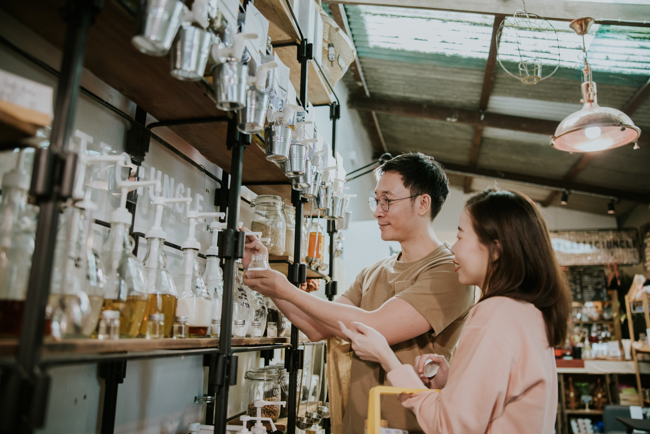 Two people are refilling laundry detergent bottles in a sustainable refill shop.