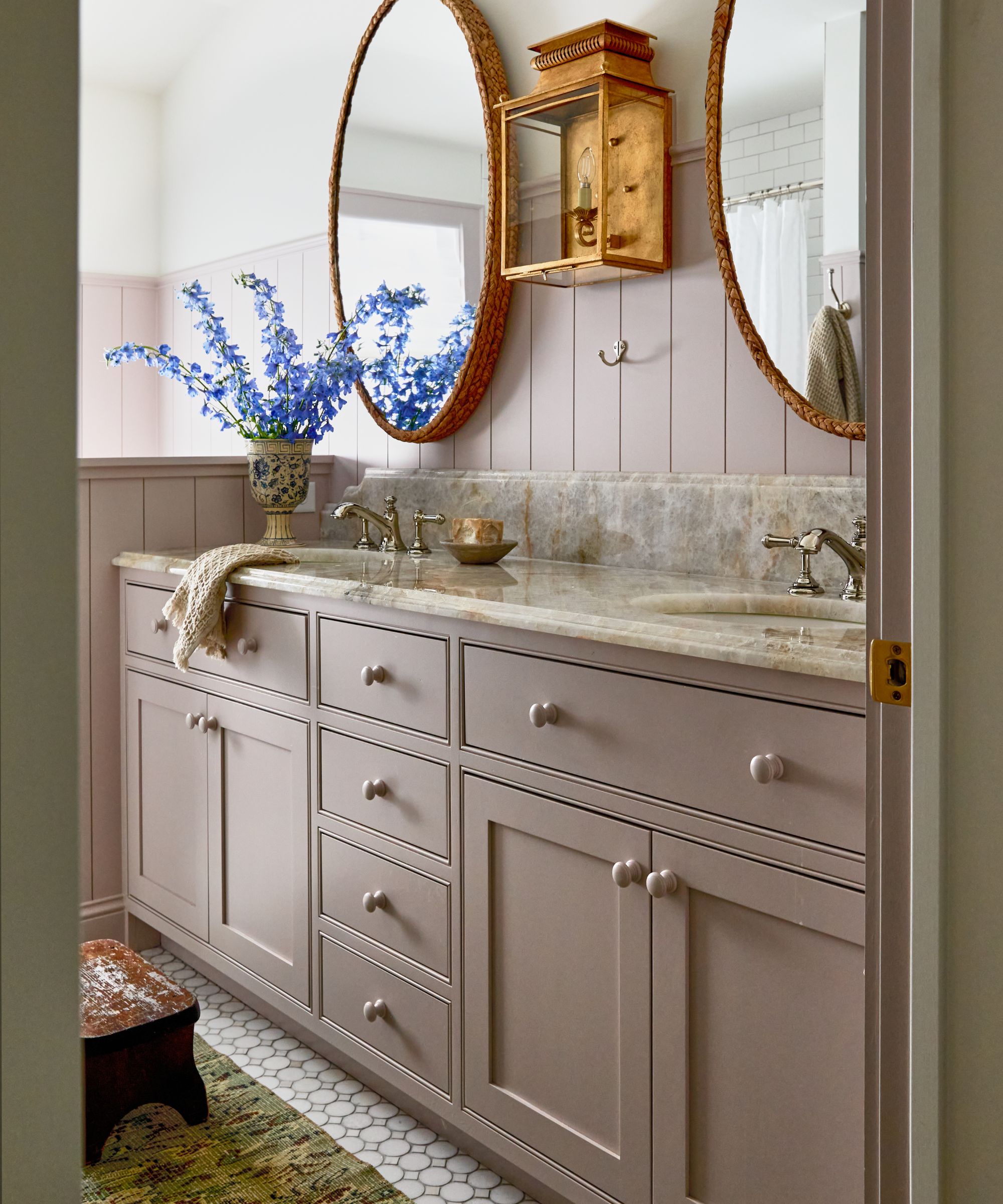 Bathroom with pink painted panelling, cabinetry, marble his and hers sinks and gold sconce