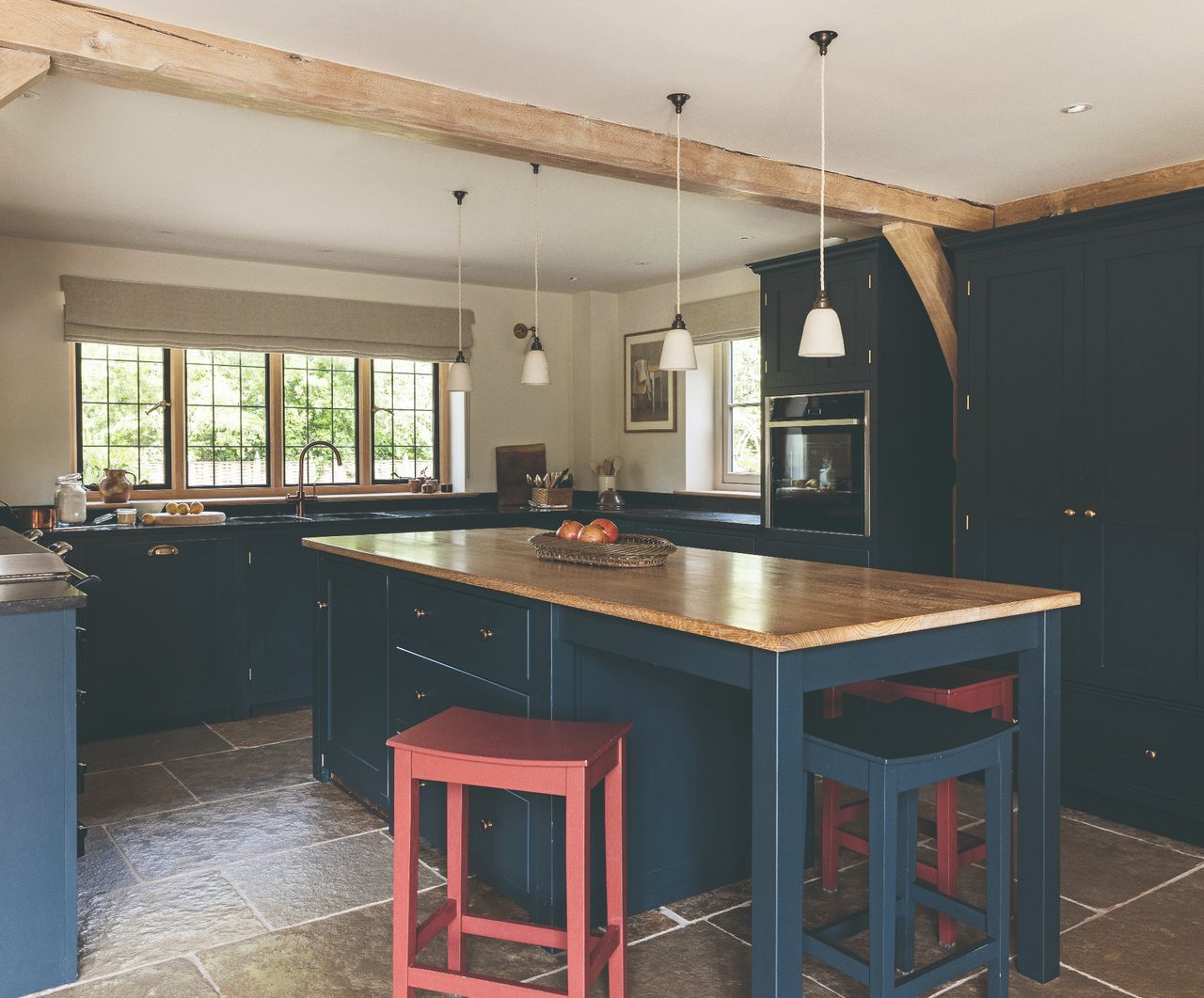 A dark blue kitchen with wooden counter tops, pendant lighting and stone tiled flooring