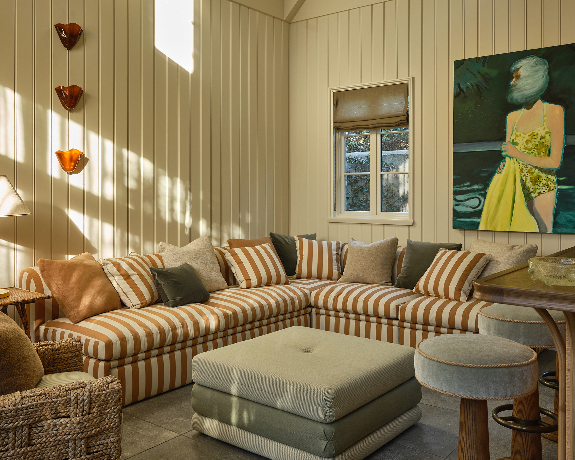 sun room with striped sofa and white wood walls and modern art on the walls