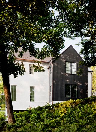 white rendered house with black clad end gable with mature trees around