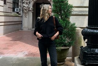 Eliza Huber wearing a black V-neck sweater, brown bag, black Citizens of Humanity Zurie black jeans, and brown shoes.