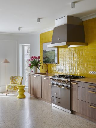 A kitchen with dark wooden cabinetry and yellow gloss tiles up the unit wall