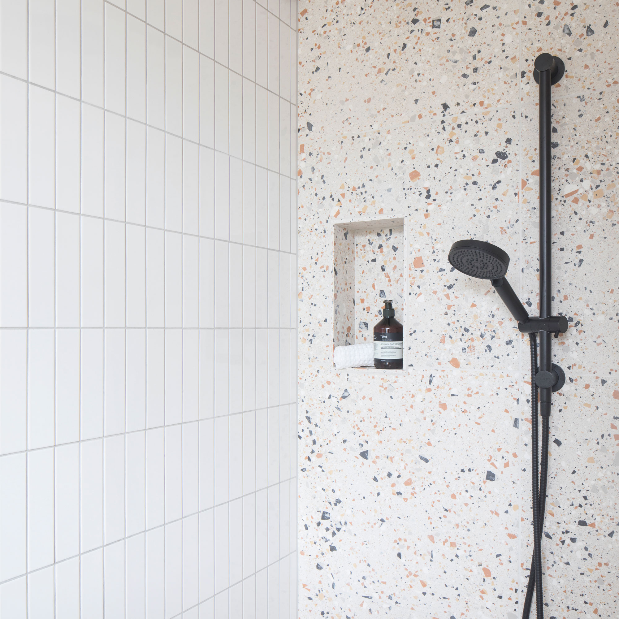 Enclosed shower with a terrazzo wall and white rectangular stacked tiles on the other wall with a black shower.