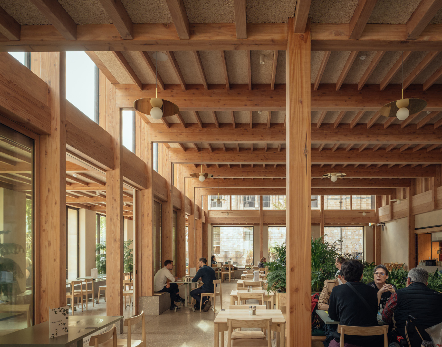 interior of timber-frame building with cafe chairs and tables, large windows and greenery