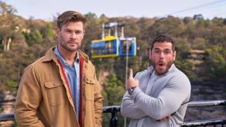 Chris Hemsworth and sports scientist Ross Edgley gaze out at a cable cart suspended over a canyon with a 100 - foot - long rope hanging from it.