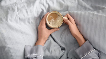 Woman holding coffee mug in bed