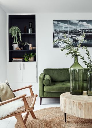 living room with white walls and green sofa with dark alcove shelving jute armchair and log coffee table