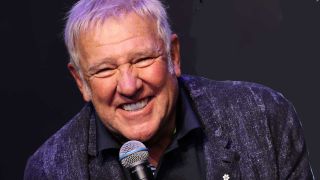 Alex Lifeson smiling while holding a microphone