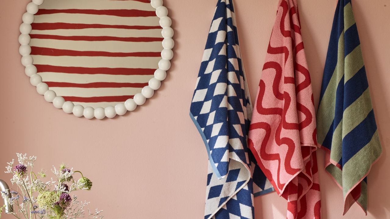 White round bobbin mirror hanging against pink wall next to patterned towels