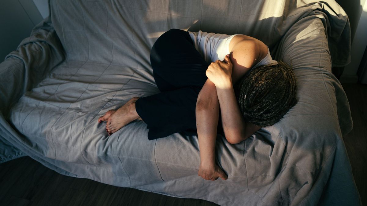 A woman curled up on the sofa napping with a bit of sunlight landing on her