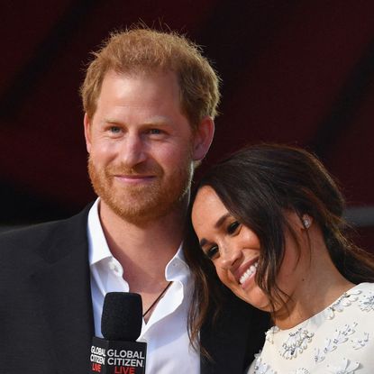 Prince Harry wears a suit jacket and an open white shirt as he hugs wife Meghan Markle at Global Citizen, she is wearing a white dress adorned with silver detailing