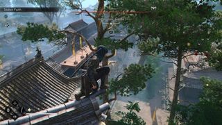 Naoe blends in among lush trees in Assassin's Creed Shadows while observing Amagasaki Castle from a rooftop perch