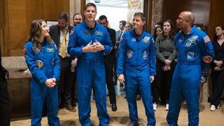 four people in blue jumpsuits in a wood-paneled hallway
