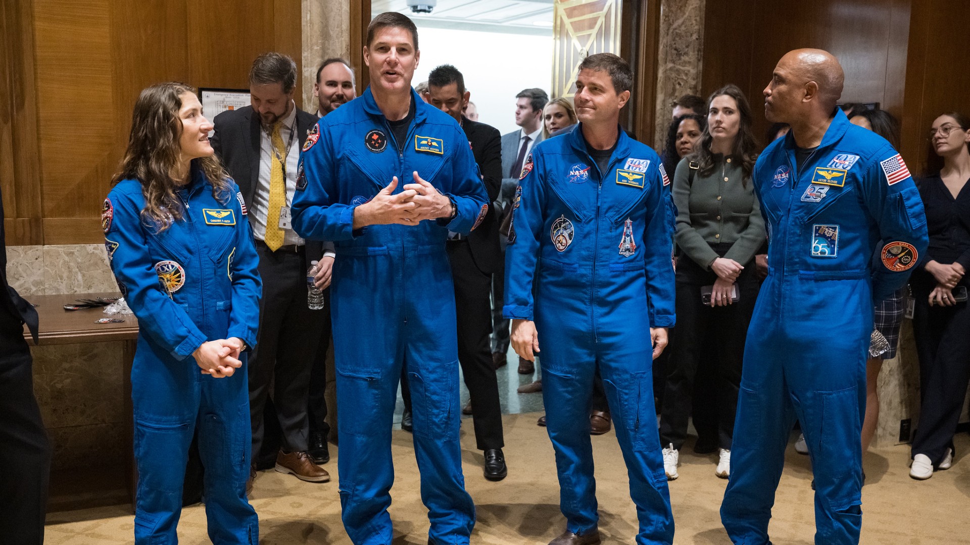 four people in blue jumpsuits in a wood-paneled hallway