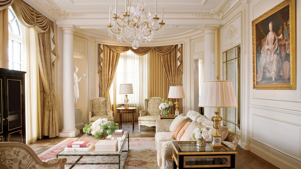 Image of traditional French-style lounge room with white walls and pillars, and gold curtains in the windows.